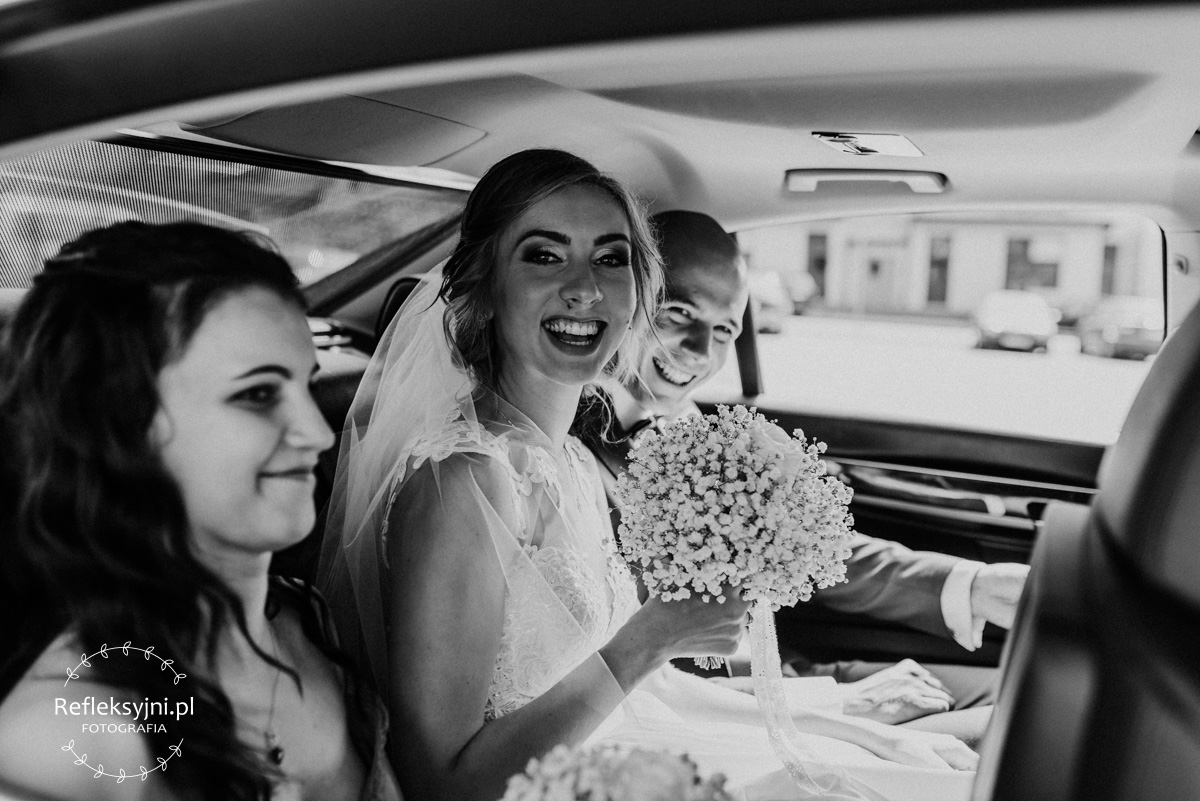 Państwo Młodzi śmiejący się w samochodzie ślubnym