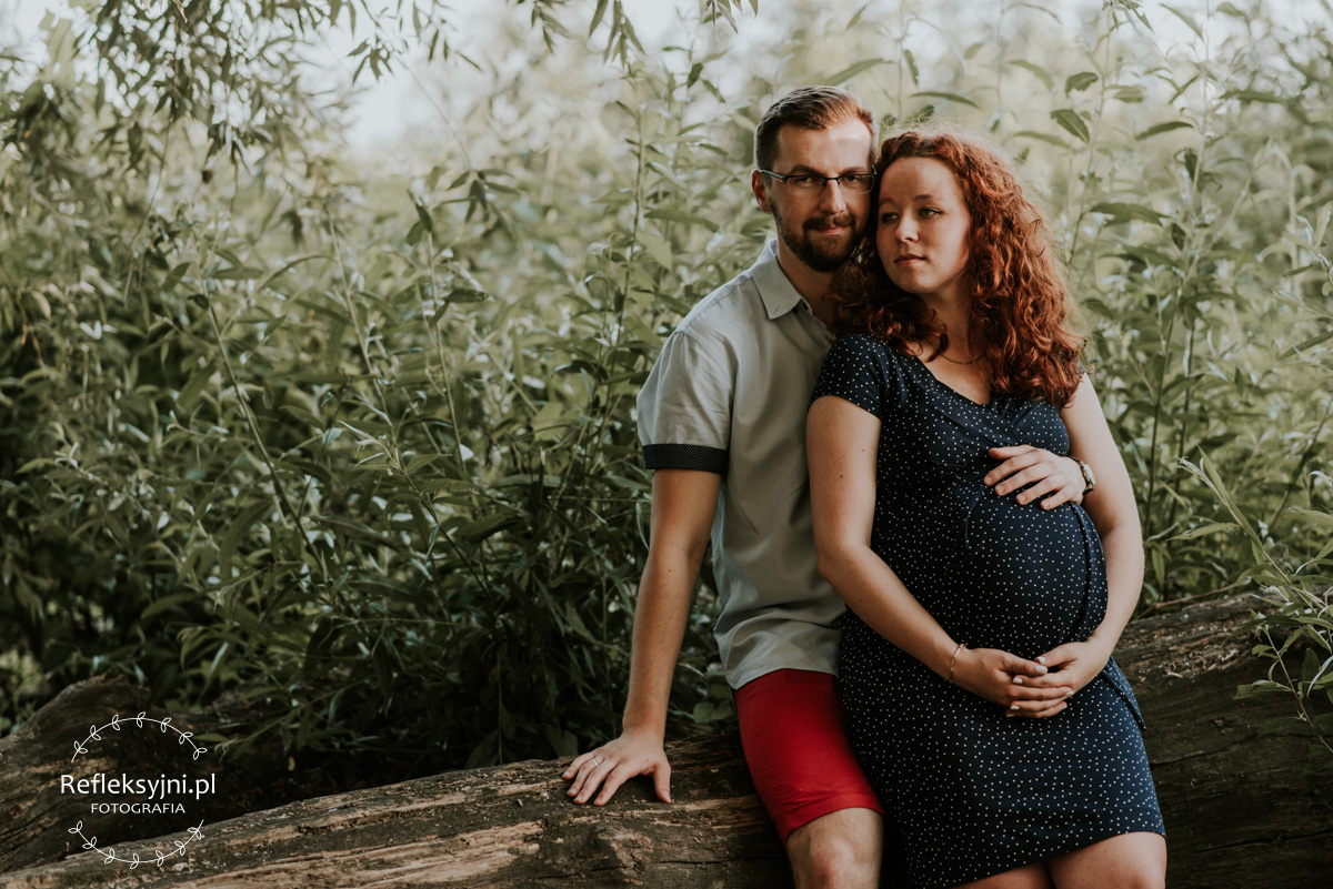 Sesja ciążowa Ruda kobieta i mężczyzna siedzą w lesie
