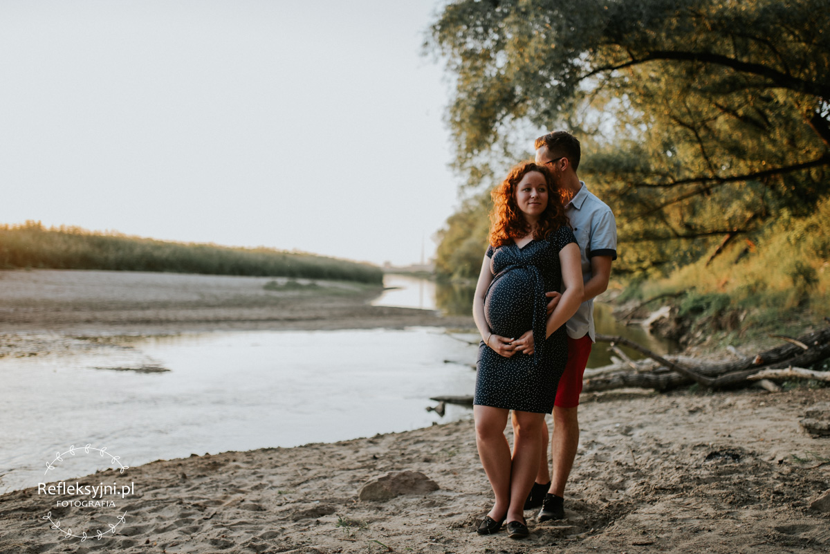 Ruda kobieta w ciąży i mężczyzna stojący na plaży nad Wisłą
